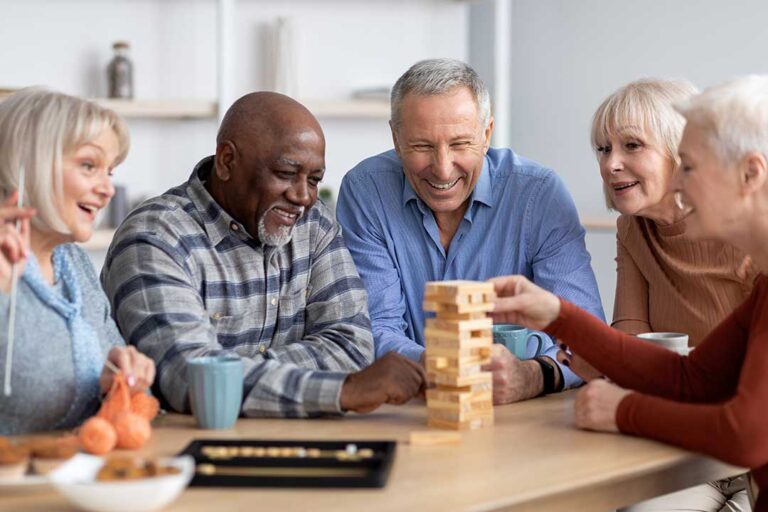 Two older adults and a family member reviewing paperwork and calculating budgets at a table in a cozy home setting.