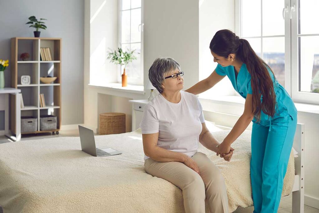 Older adult choosing clothing in a bright assisted living apartment with a caregiver offering light support.